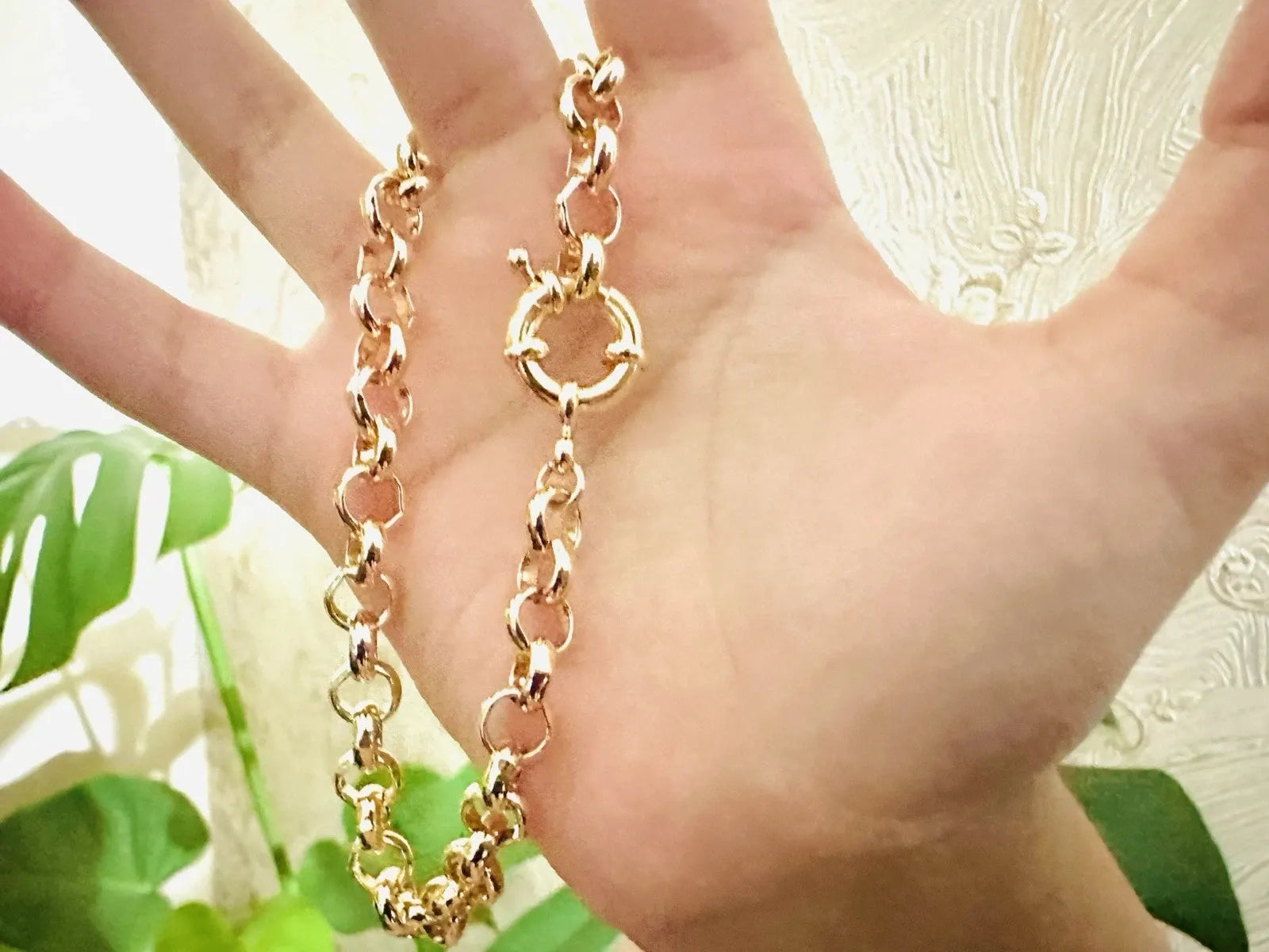 Gold chain held between fingers with a blurred natural background