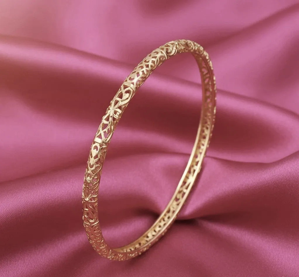 Gold bracelet with intricate design on a pink satin background