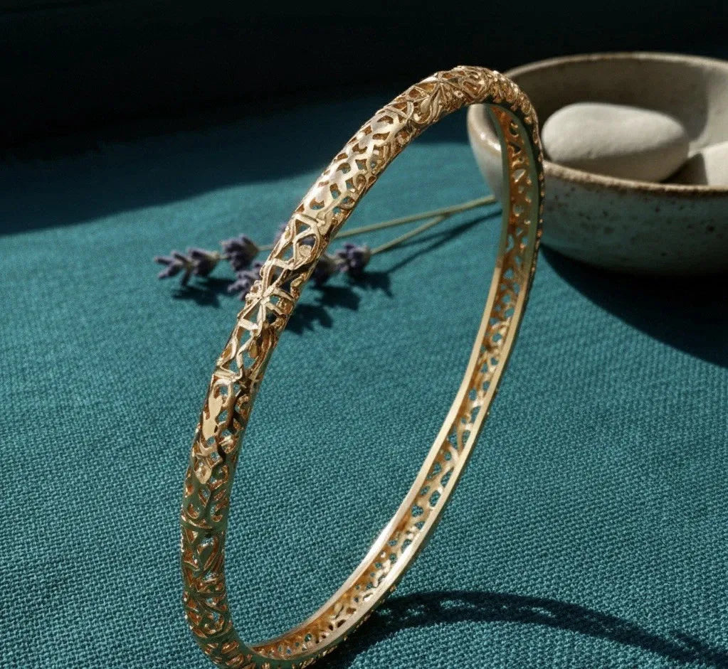 Gold bracelet on a teal surface with a bowl and lavender flowers in the background