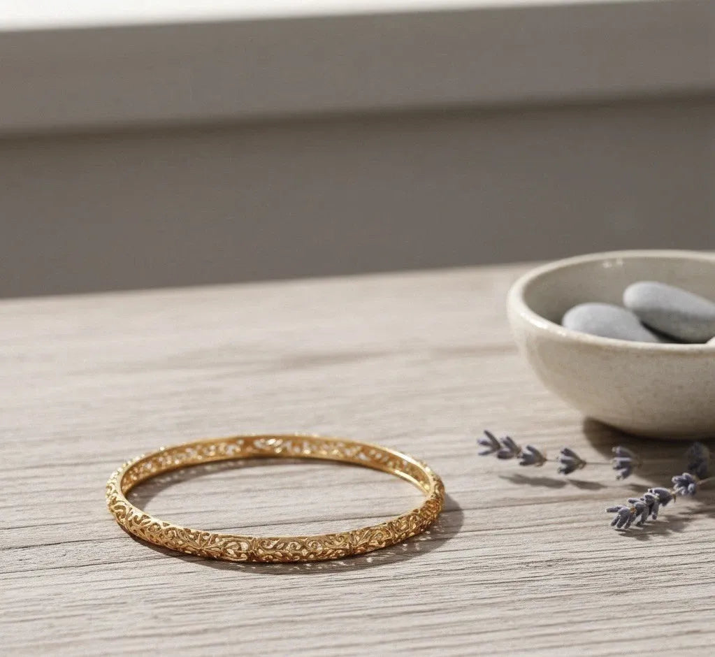 Gold bracelet on a wooden surface with a bowl of stones and lavender in the background.