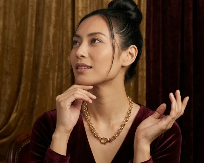 Woman wearing a gold necklace against a warm-toned curtain background